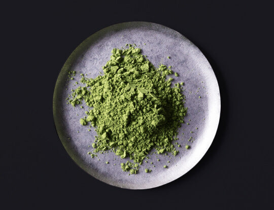 loose bright green finely ground milled Ippodo Tea Co. Japanese Matcha tea powder on silver plate on black table