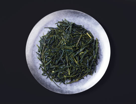 Loose leaf dark green rolled dried Ippodo Tea Co. Sencha premium Japanese green tea on silver plate on black background