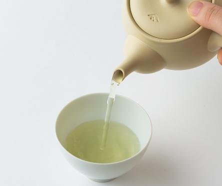 Pouring futsumuchi roasted green tea Hojicha from Ivory Tokoname-yaki ceramic (kyusu) teapot into white porcelain teacup
