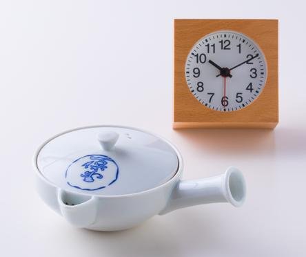 Small white porcelain Japanese kyusu teapot with blue logo on lid sitting beside orange stop watch timer on white table