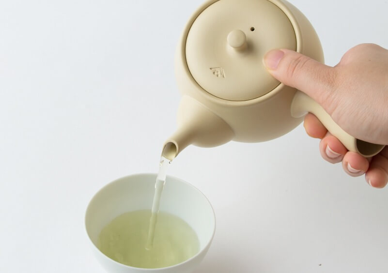 Pouring green tea from ivory Tokoname-yaki ceramic kyusu teapot into small white porcelain Japanese teacup