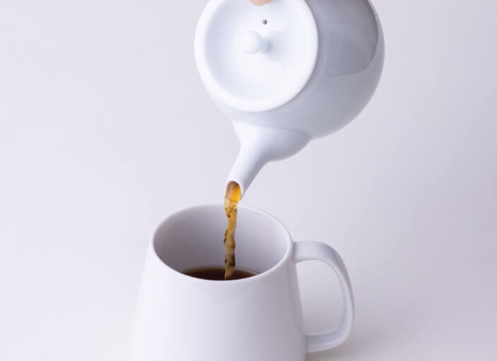Pouring amber Hojicha roasted green tea from white Hakuji ceramic (kyusu) teapot into white porcelain Japanese teacup