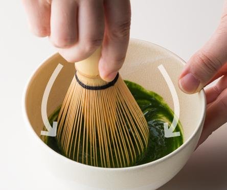 Whisking dark green thick matcha in tea bowl using Chasen bamboo whisk and overlaid directions arrows along sides of bowl