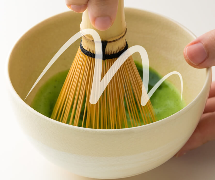 Whisking vibrant green matcha tea in ceramic tea bowl using Chasen bamboo whisk with zigzag 