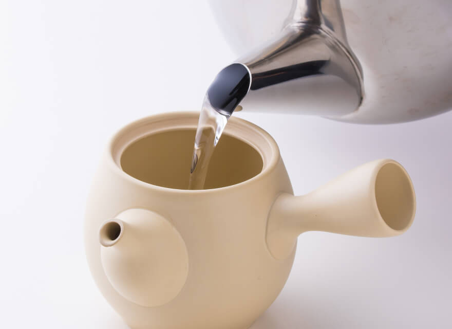 Pouring water from glass carafe into white porcelain Hasami-yaki teapot containing Gyokuro green tea leaves and ice cubes