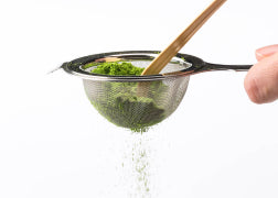 Vibrant green Ippodo matcha powder being sifted through Chakoshi tea strainer with Chashaku bamboo tea ladel