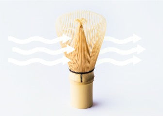 Bamboo chasen whisk air drying while standing on end with wavy white arrows flowing over tips indicating air flow through
