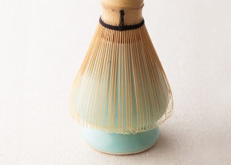 Close-up of light pastel turquoise blue Ippodo Tea ceramic whisk stand supporting Japanese bamboo matcha whisk 80-tip Chasen
