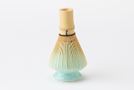 Bamboo chasen resting tips-down on a pale blue ceramic whisk stand