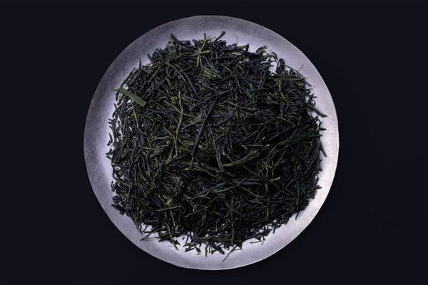 Loose leaf dark green rolled dried Ippodo Tea Co. Gyokuro premium Japanese green tea on silver plate on black background