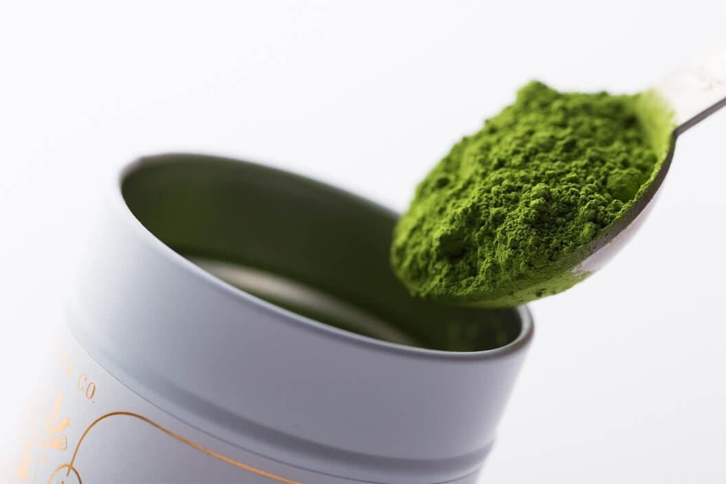 Modern brushed silver tablespoon scooping verdant vibrant green fine ground matcha powder from white metal Ippodo Tea tin
