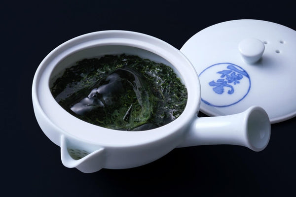 Large lush verdant dark Japanese green tea leaves brewing in small portion of gyokuro tea in small ceramic Japanese kyusu teapot