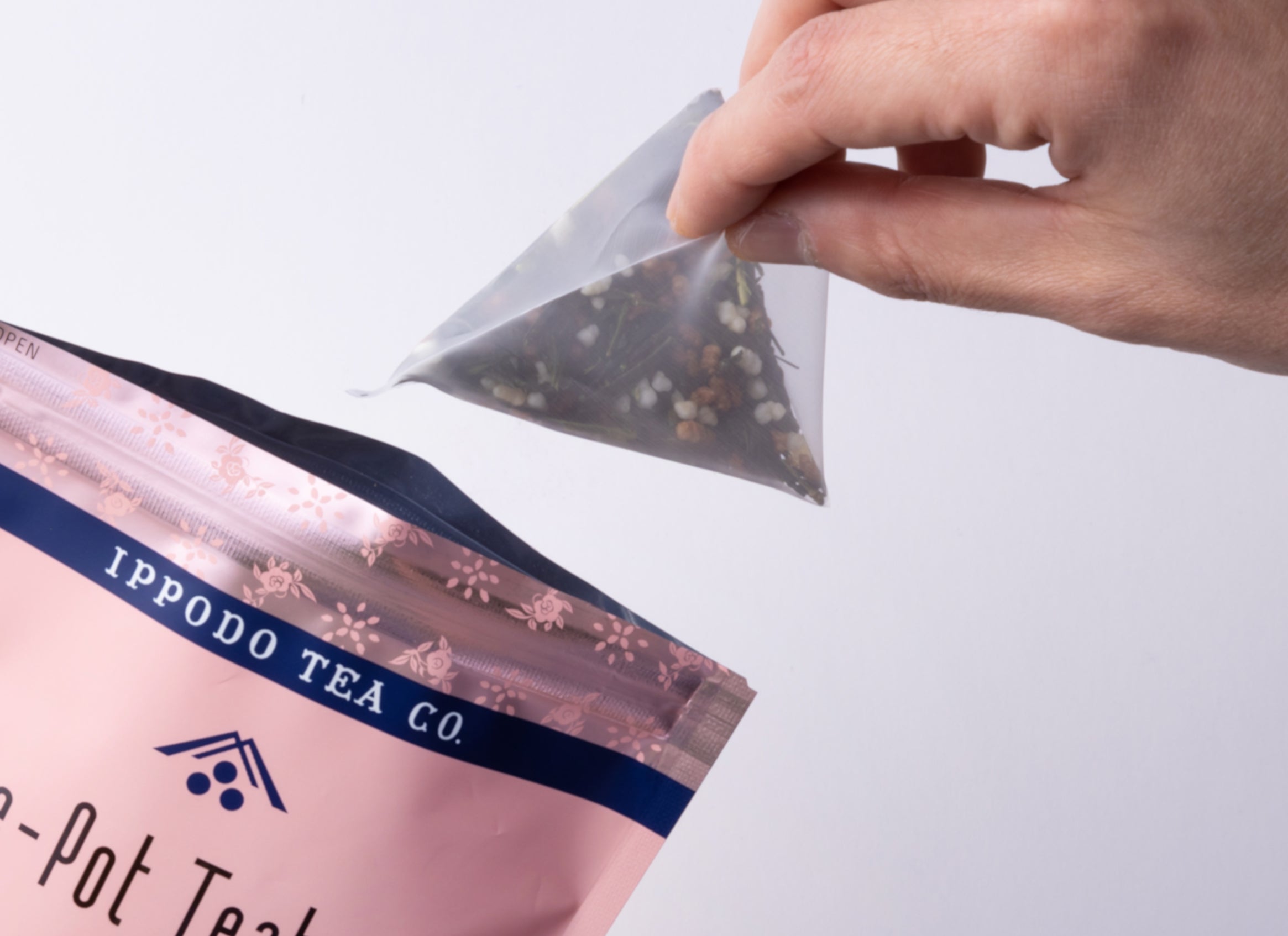 A hand pulling one pyramid-shaped genmaicha teabag from package - Genmaicha Teabags - Hot Brew