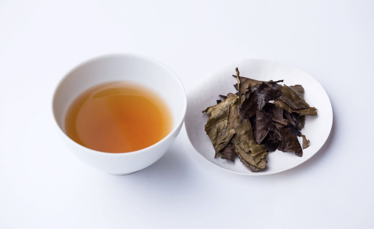 Iribancha tea brewed in a white cup with a plate of loose leaf iribancha next to it