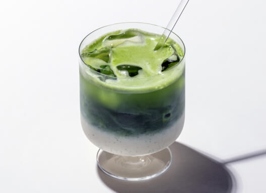 Short stemmed glass with decadent layered green matcha and milk with ice and glass straw