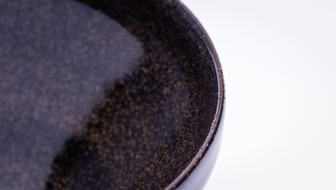 Sleek shiny cone shaped speckled black glazed ceramic matcha tea bowl with light-colored unglazed base