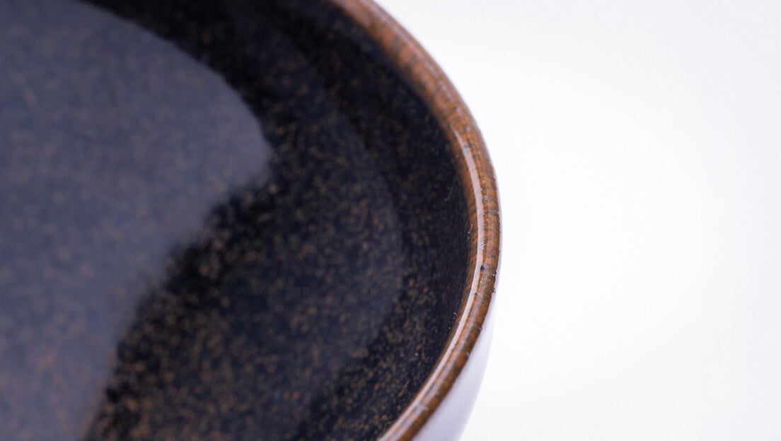 Sleek shiny cone shaped speckled black glazed ceramic matcha tea bowl with light-colored unglazed base