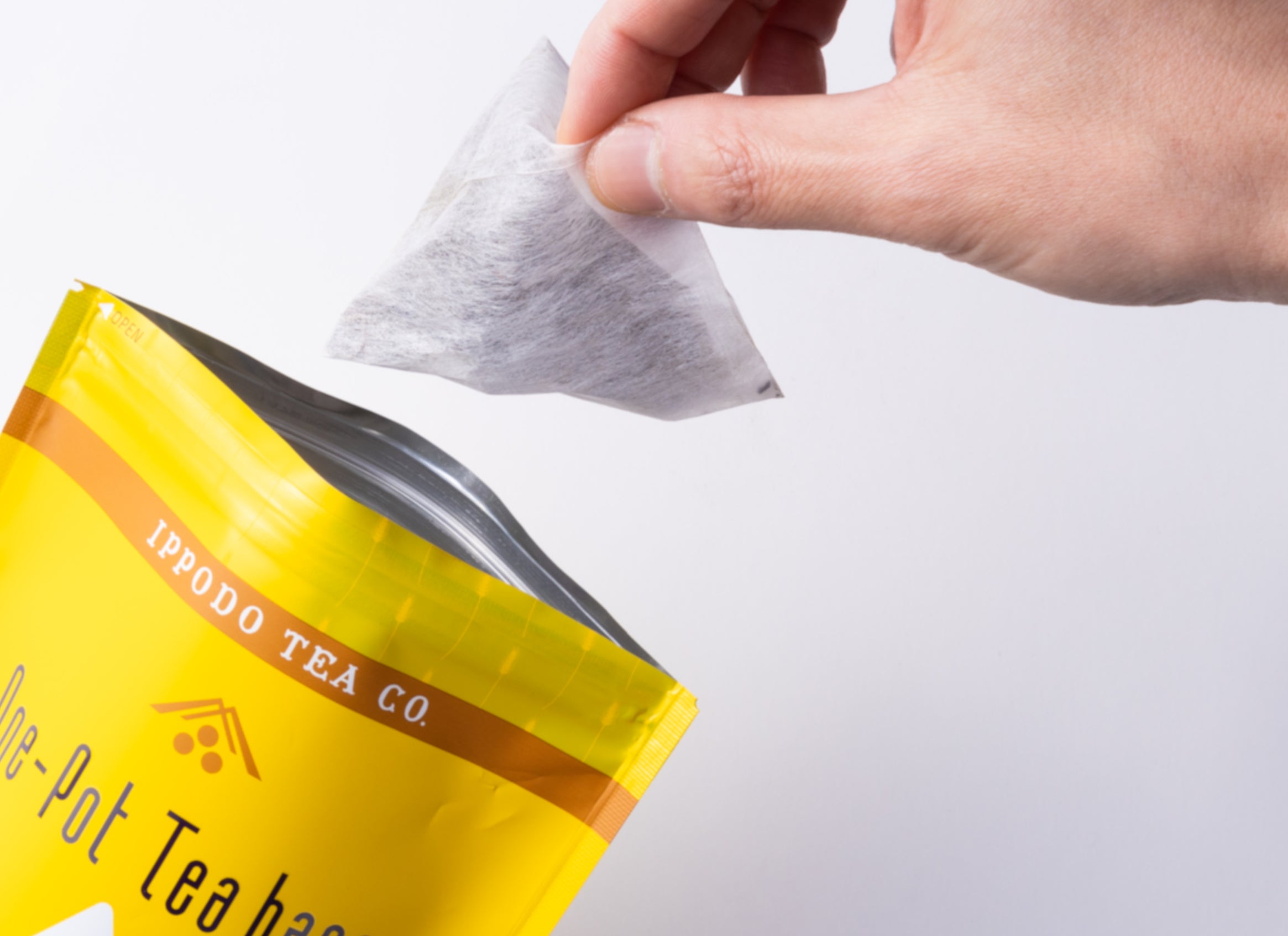 Hand removing one pyramid-shaped mugicha teabag from packaging - Mugicha Teabags - Hot Brew