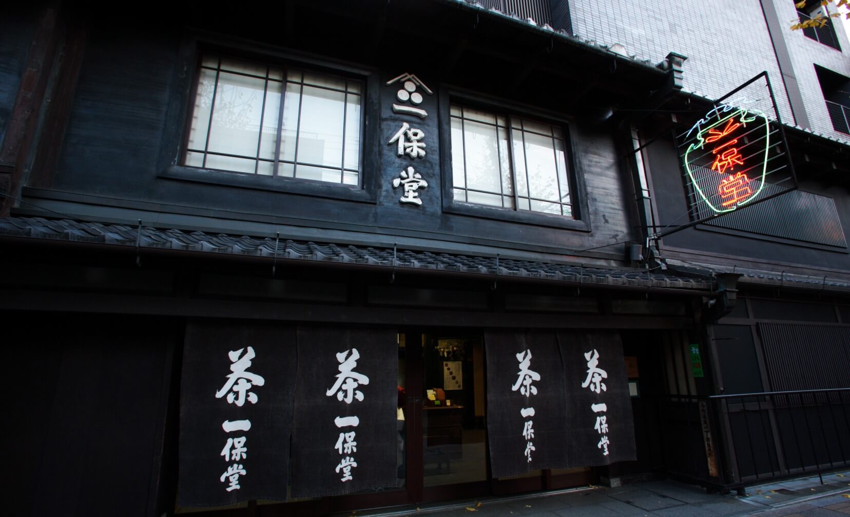 Front of of Ippodo Tea's flagship store, tearoom and headquarters black storefront in Kyoto, Japan with outdoor lit neon sign