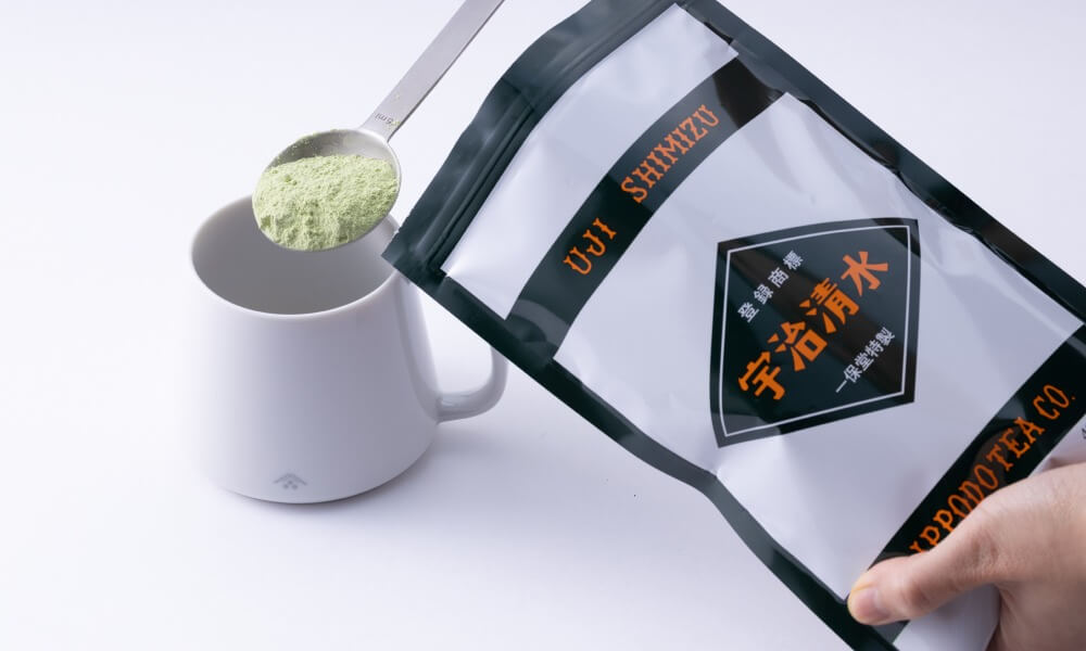 Picture of a bag of uji-shimizu sweetened matcha powder being scooped into a white mug